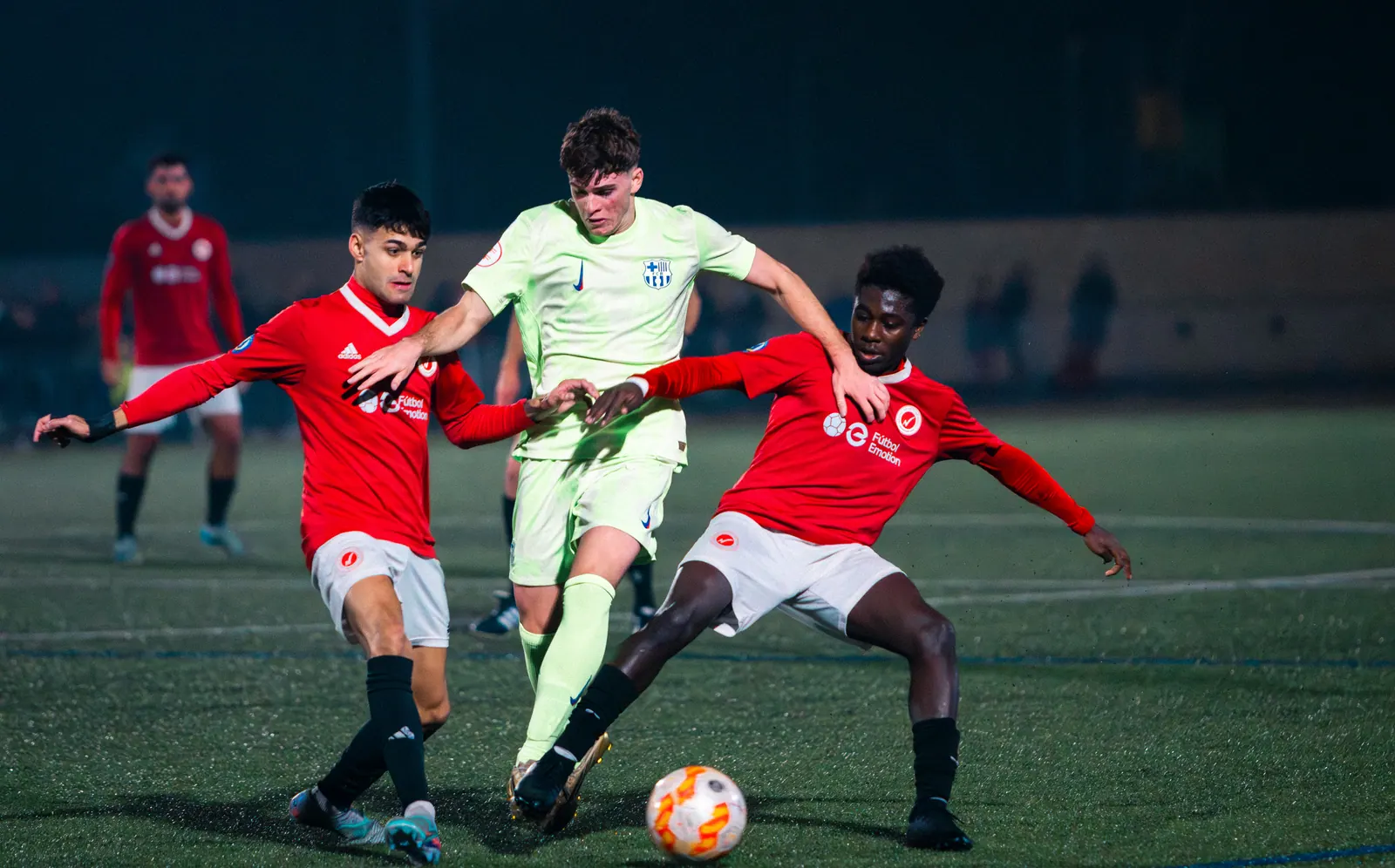 A player shielding the ball from two defenders in a night match