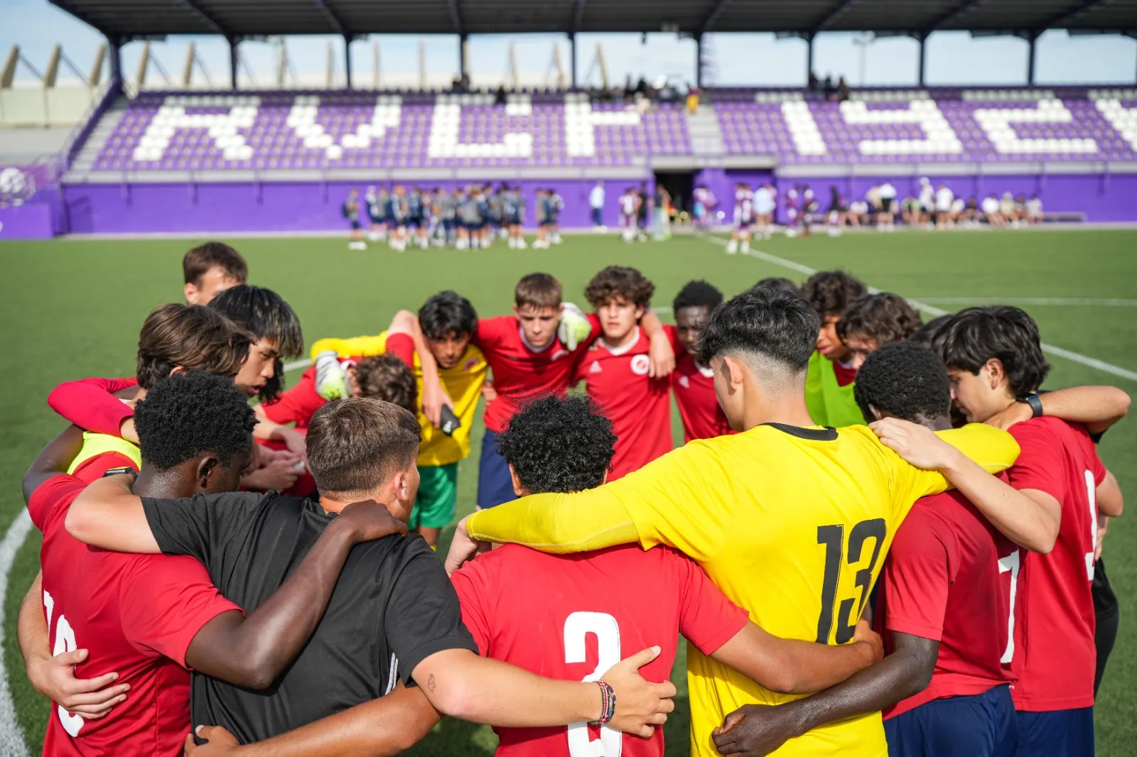 A team huddle on the pitch inside a stadium